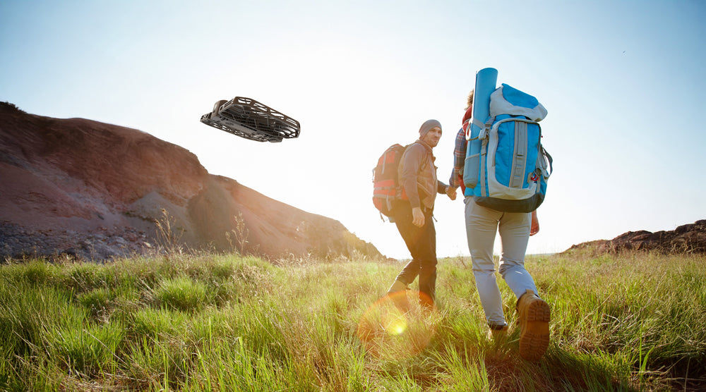 Hikers using HOVERAir X1 lightweight camera drone on a sunny outdoor trail.